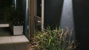 A building exterior at night with illuminated wall lights, a door, and potted plants.