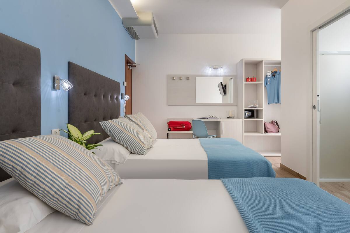 A modern bedroom with two beds, a desk, and a wardrobe.