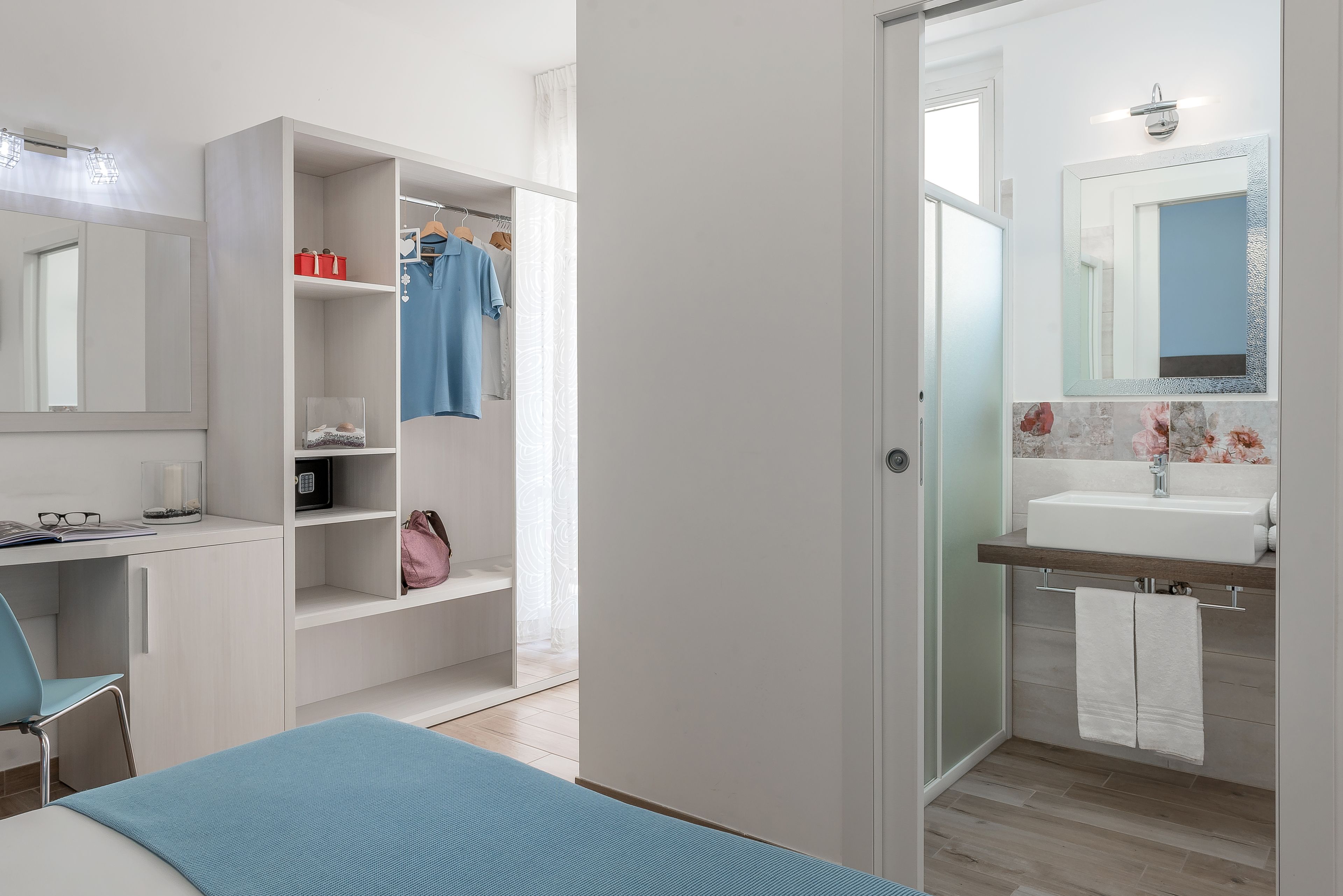 Une chambre moderne comprenant un lit, un bureau, une armoire et une salle de bain avec un lavabo et un miroir.