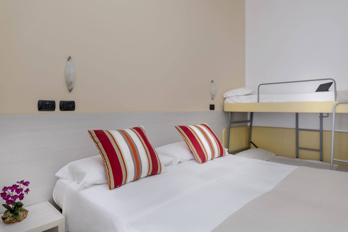 A hotel room with a bunk bed, a bedside table with a vase of flowers, and a wall-mounted light fixture.