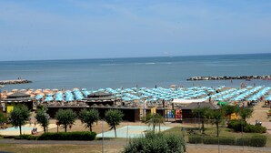 A beach resort with numerous umbrellas and beach chairs, a pool area, and a view of the sea.