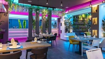 Een modern restaurant met tafels, stoelen, neonverlichting en hangplanten.