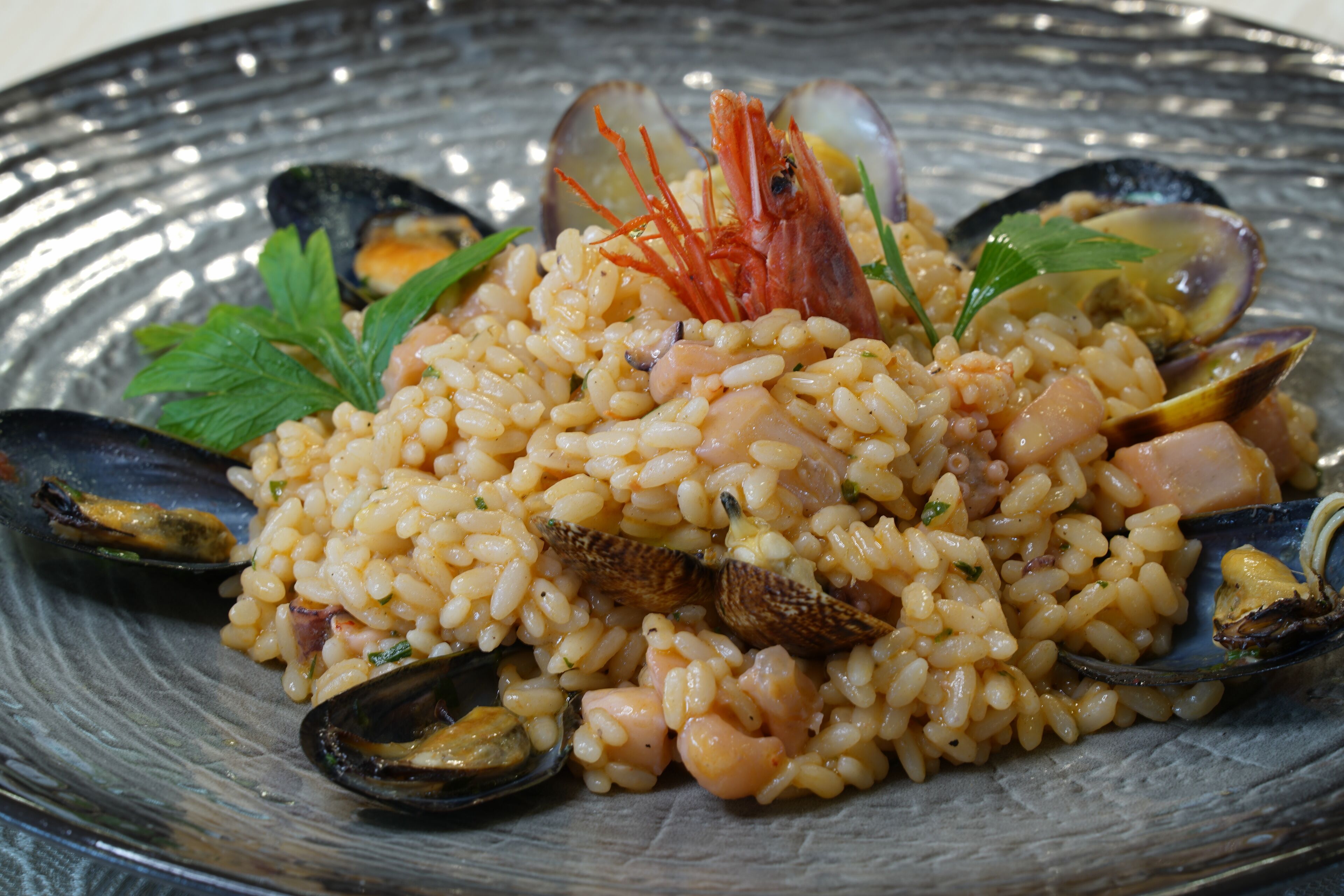 Un plat de risotto aux fruits de mer, agrémenté de moules et de crevettes, servi dans une assiette en verre.