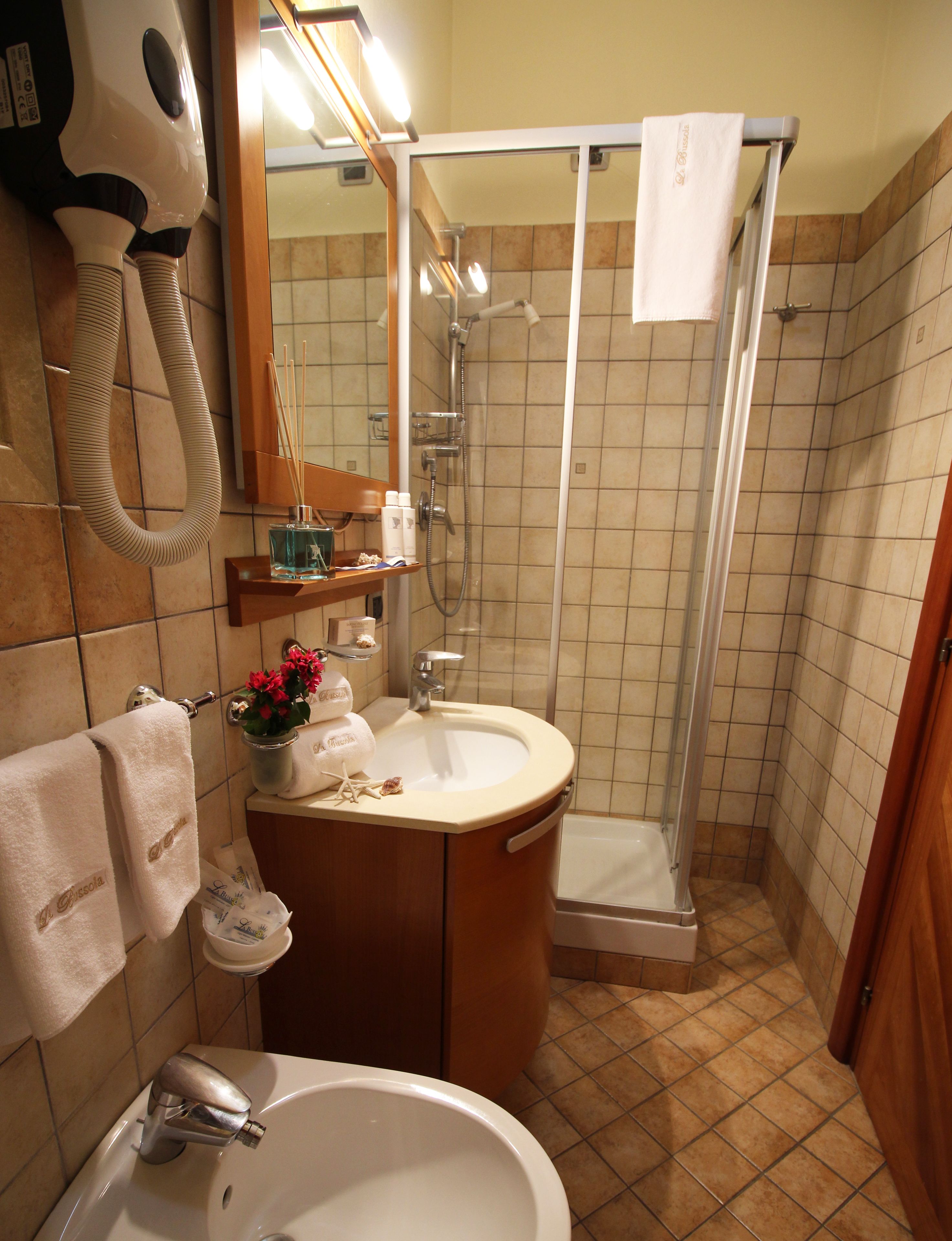 A bathroom with a sink, mirror, towel rack, shower, and toiletries.