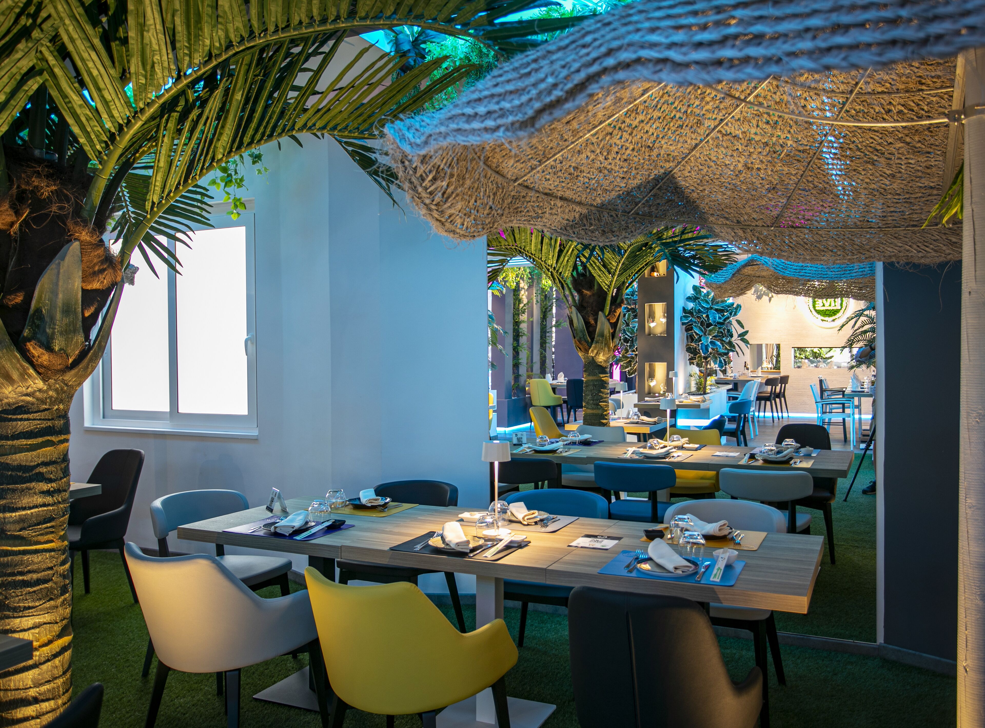 Restaurante com mesas internas, piscina e decoração tropical.