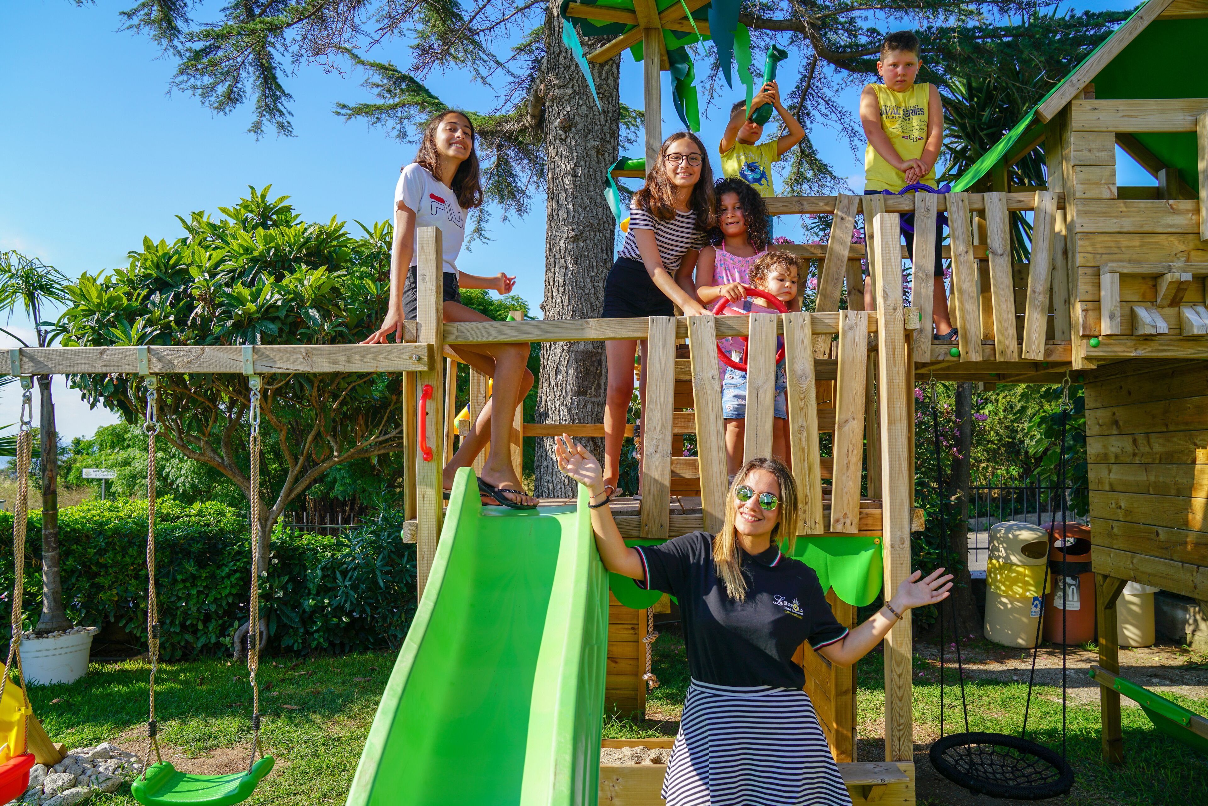A wooden play structure with a green slide, rope swings, and a small bridge.