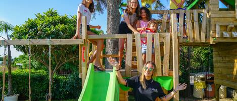 A wooden play structure with a green slide, rope swings, and a small bridge.