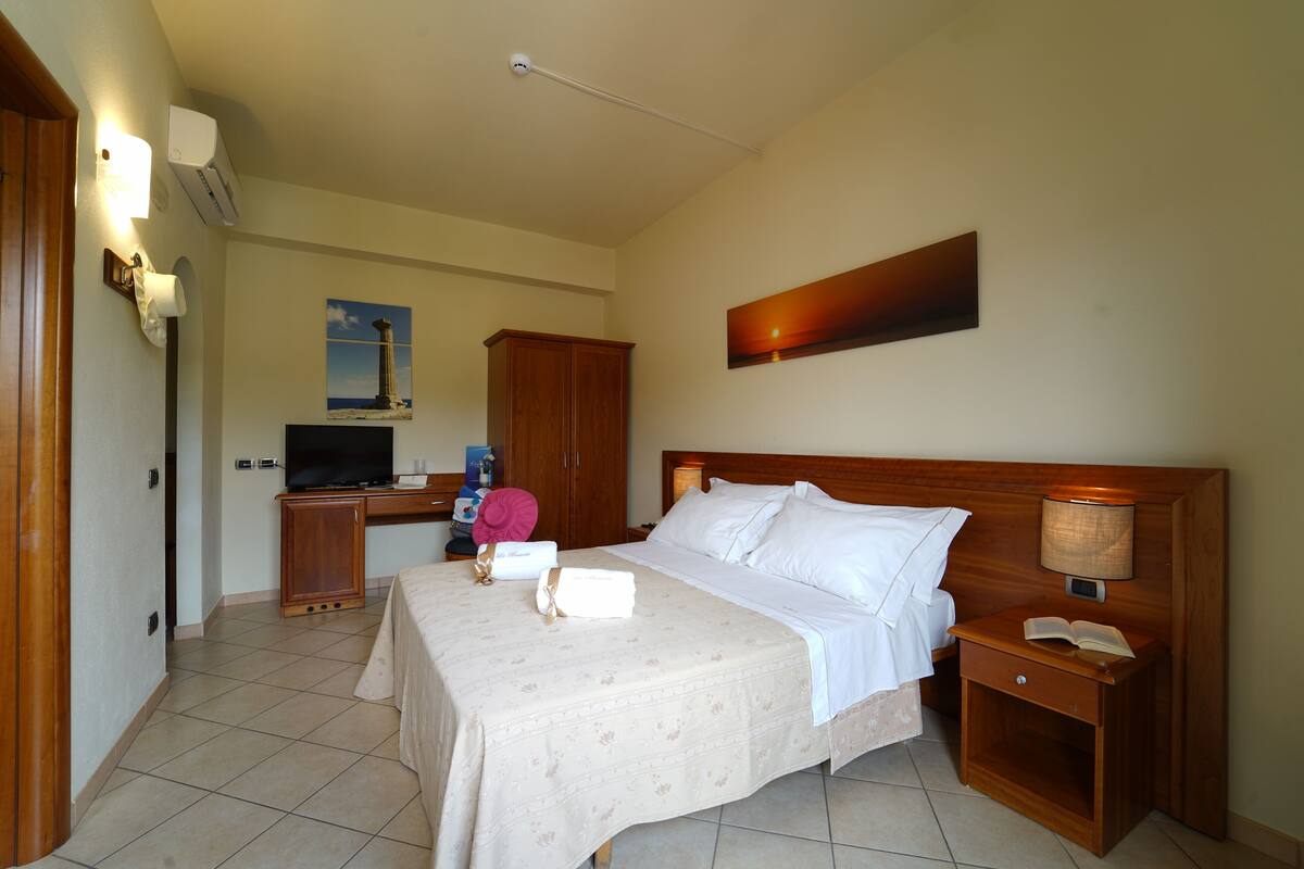Ein Hotelzimmer mit einem Bett, einem Schreibtisch mit Computer, einem Fernseher und einem Bild an der Wand.
