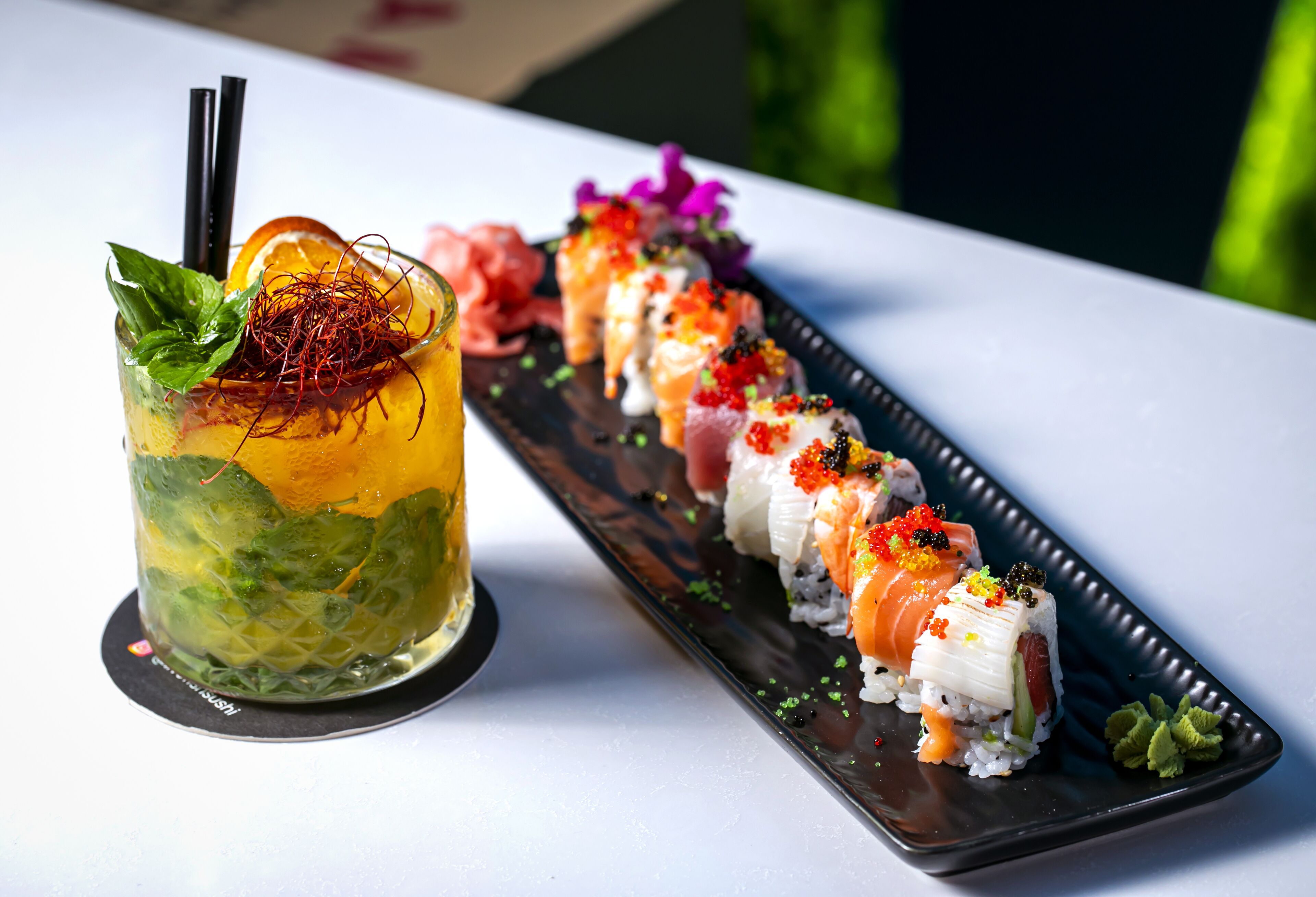 A sushi platter with various types of sushi and a cocktail with a mint garnish.