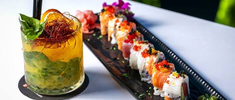 A sushi platter with various types of sushi and a cocktail with a mint garnish.