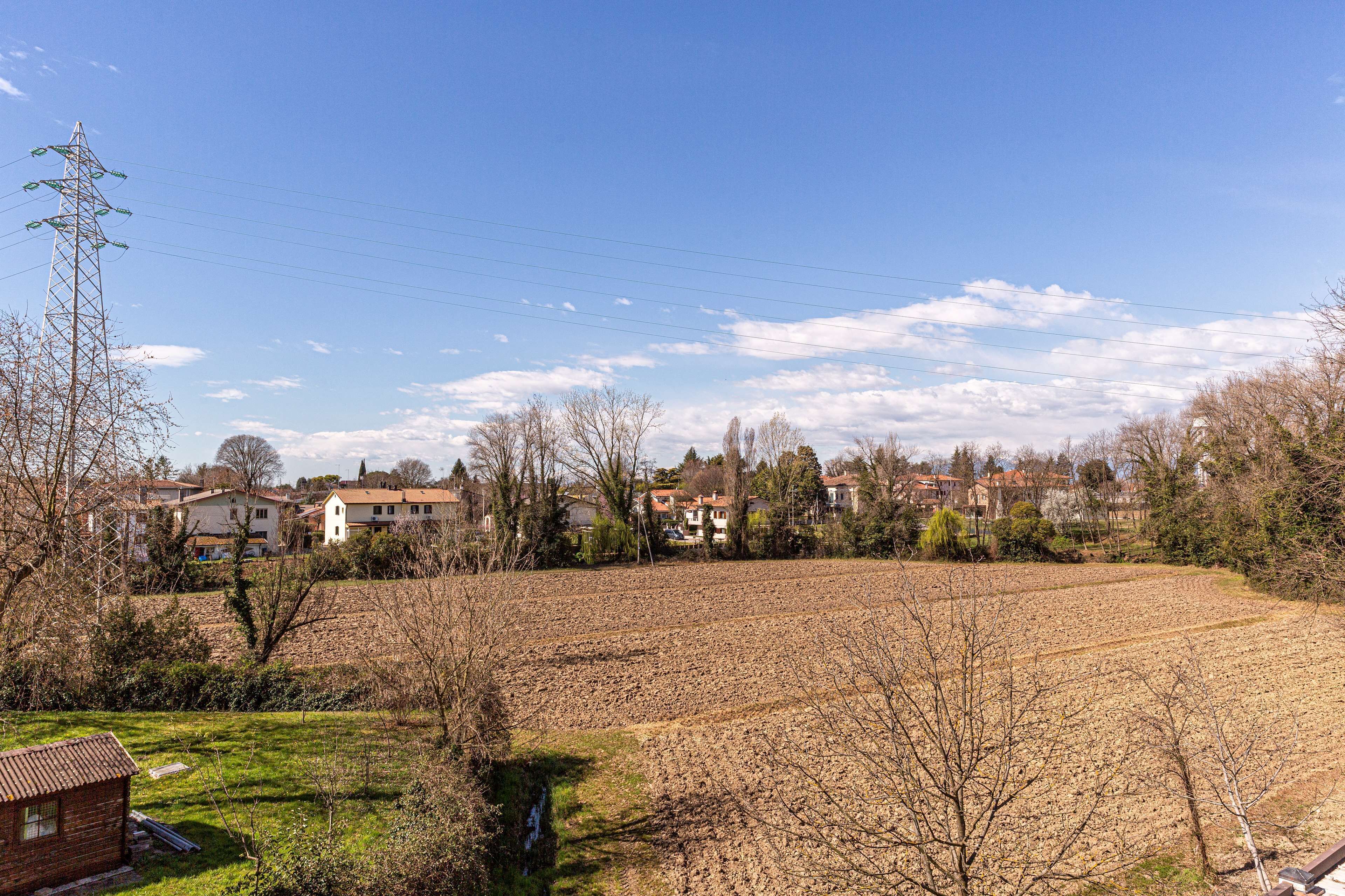 Ländliche Landschaft mit einem großen, offenen Feld, einigen Häusern und einem Strommasten.