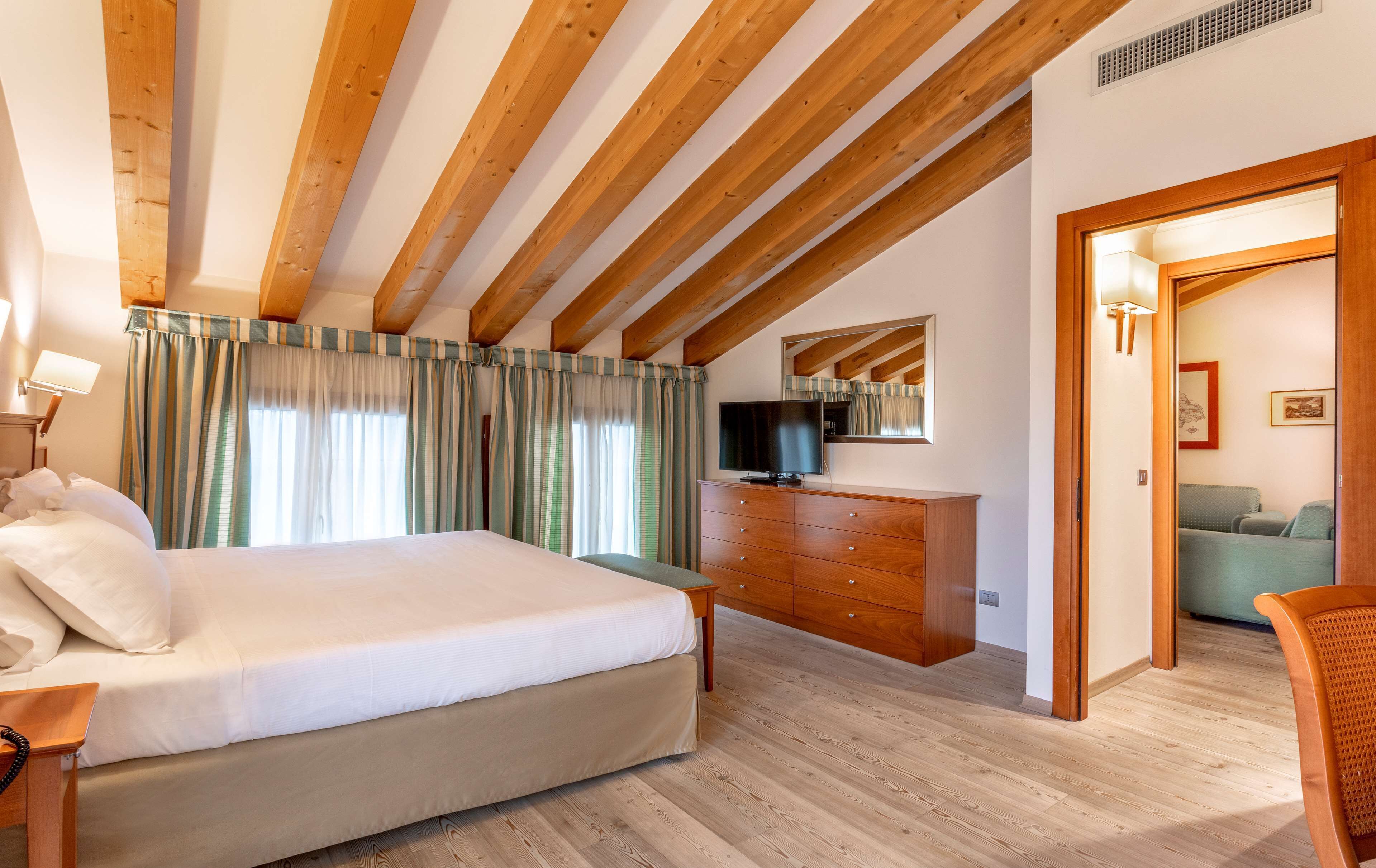 A bedroom with a wooden ceiling, a bed, a dresser, a television, and a door leading to another room.