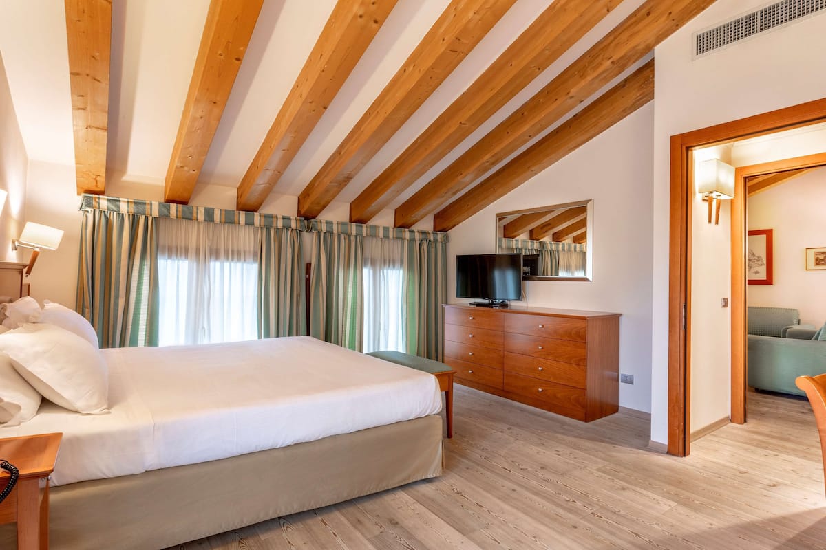 A bedroom with a wooden ceiling, a bed, a dresser, a television, and a door leading to another room.