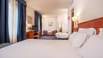 A hotel room with a large bed, a desk with a chair, a small table, two armchairs, a sofa, and a large window with curtains.