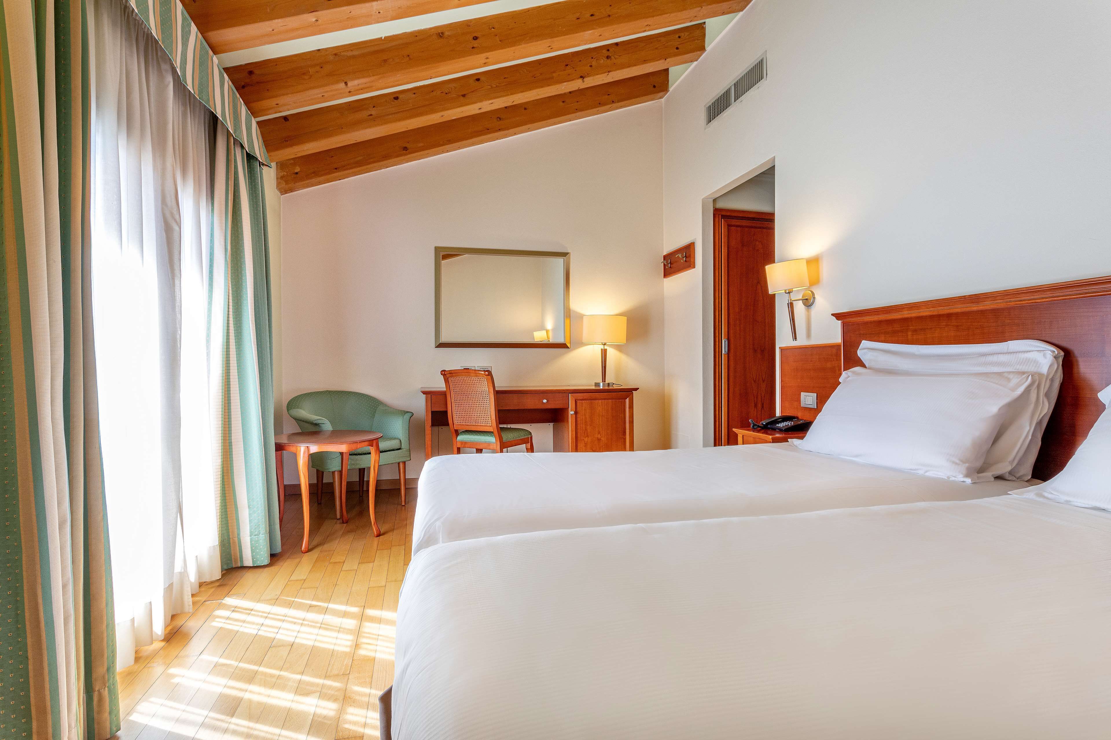 A hotel room with two beds, a desk, a chair, a lamp, and a mirror.
