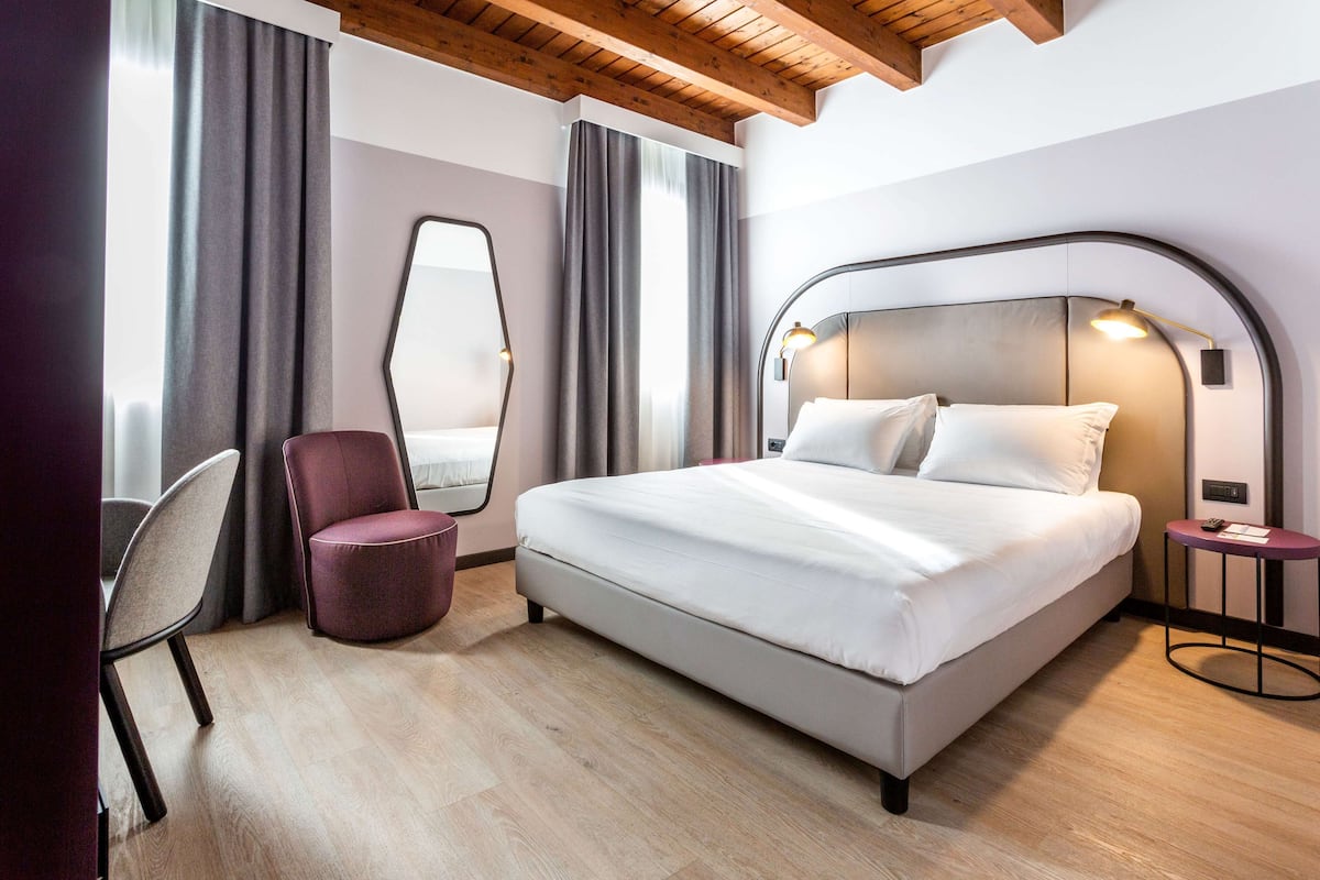 A modern hotel room with a large bed, a chair, a round table, and a mirror.