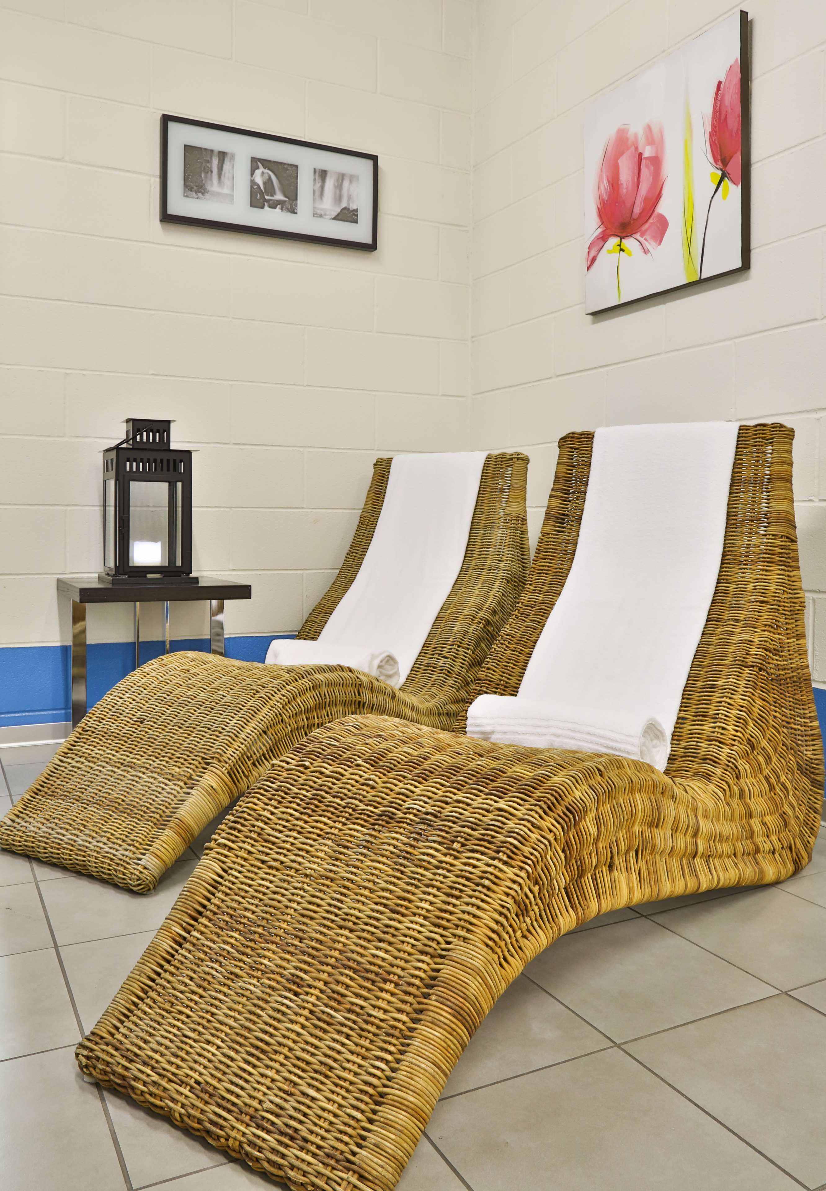 Una stanza con un divano in rattan intrecciato, un tavolino con una lanterna e una cornice con una foto appesa al muro.