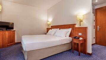 Quarto de hotel com uma cama grande, televisão, mesa de cabeceira com abajur e armário de madeira.