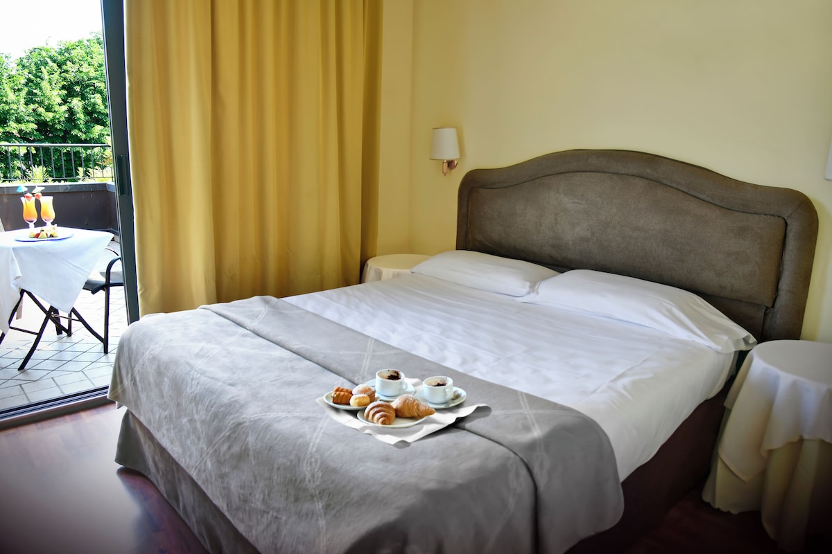 A hotel room with a bed, a dining table with breakfast, and a balcony with a table and chairs.