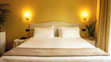 A hotel room with a large bed, two bedside lamps, a nightstand with a phone, and a potted plant.