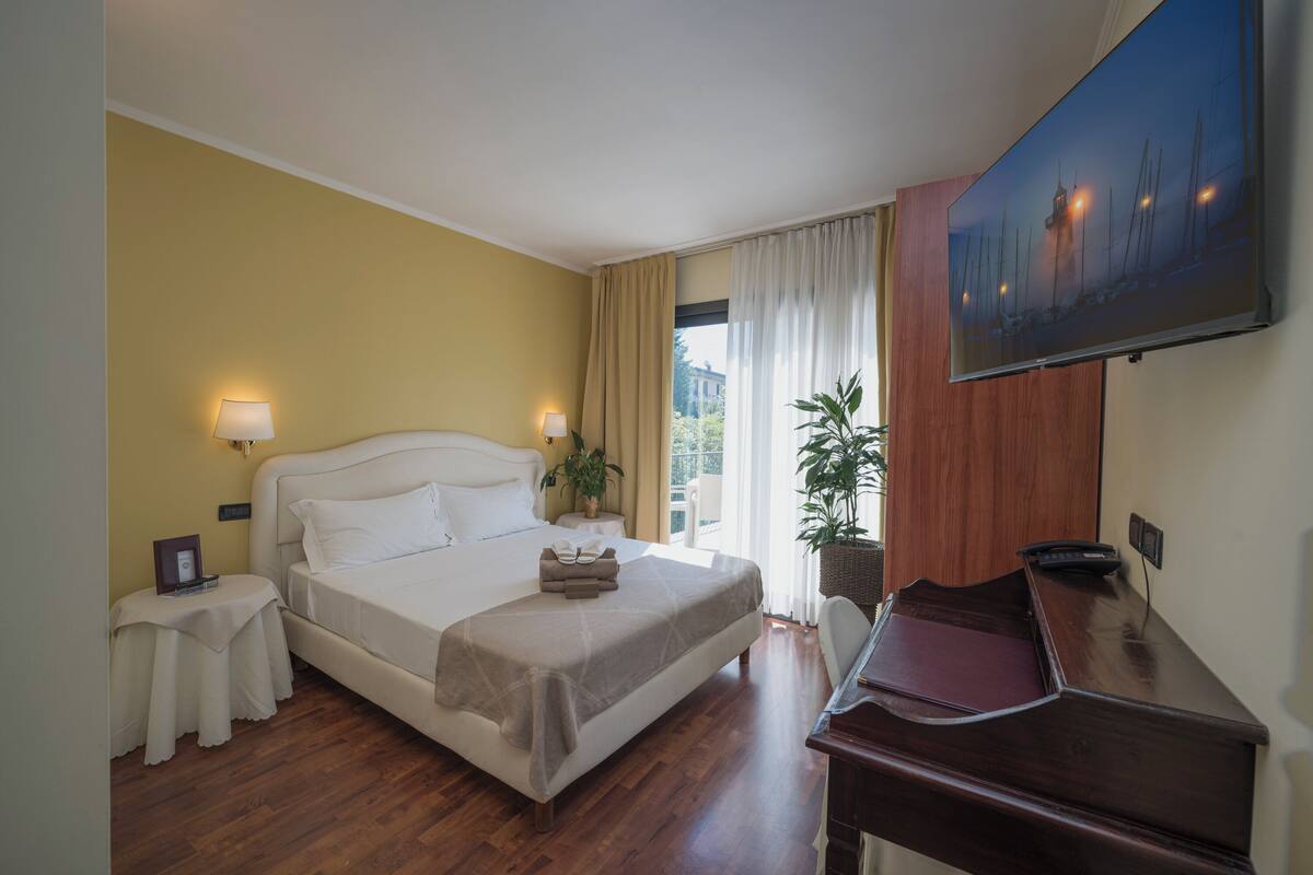 Habitación de hotel con cama, mesitas de noche, escritorio, silla, televisor y ventana con cortinas.