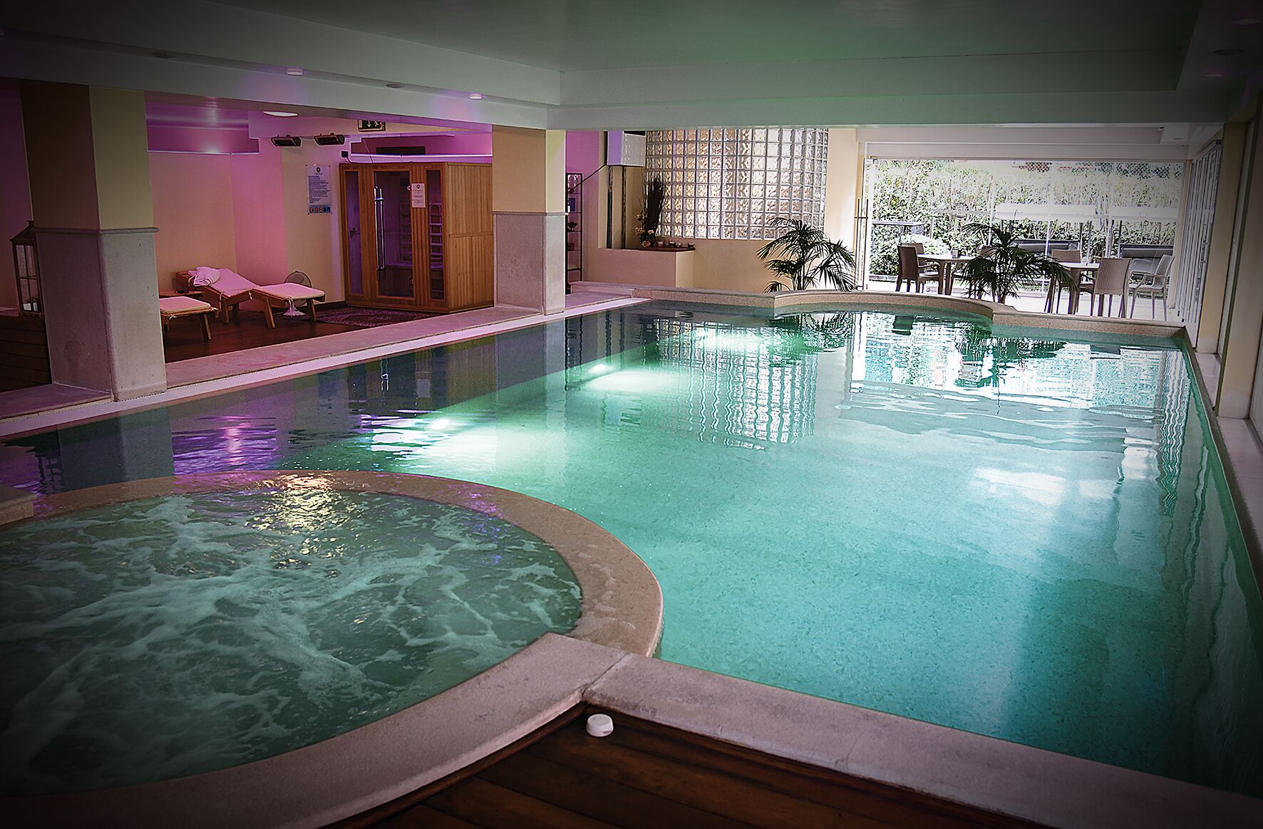 Une piscine intérieure dotée d’un jacuzzi, de chaises longues et offrant une vue sur l’extérieur.