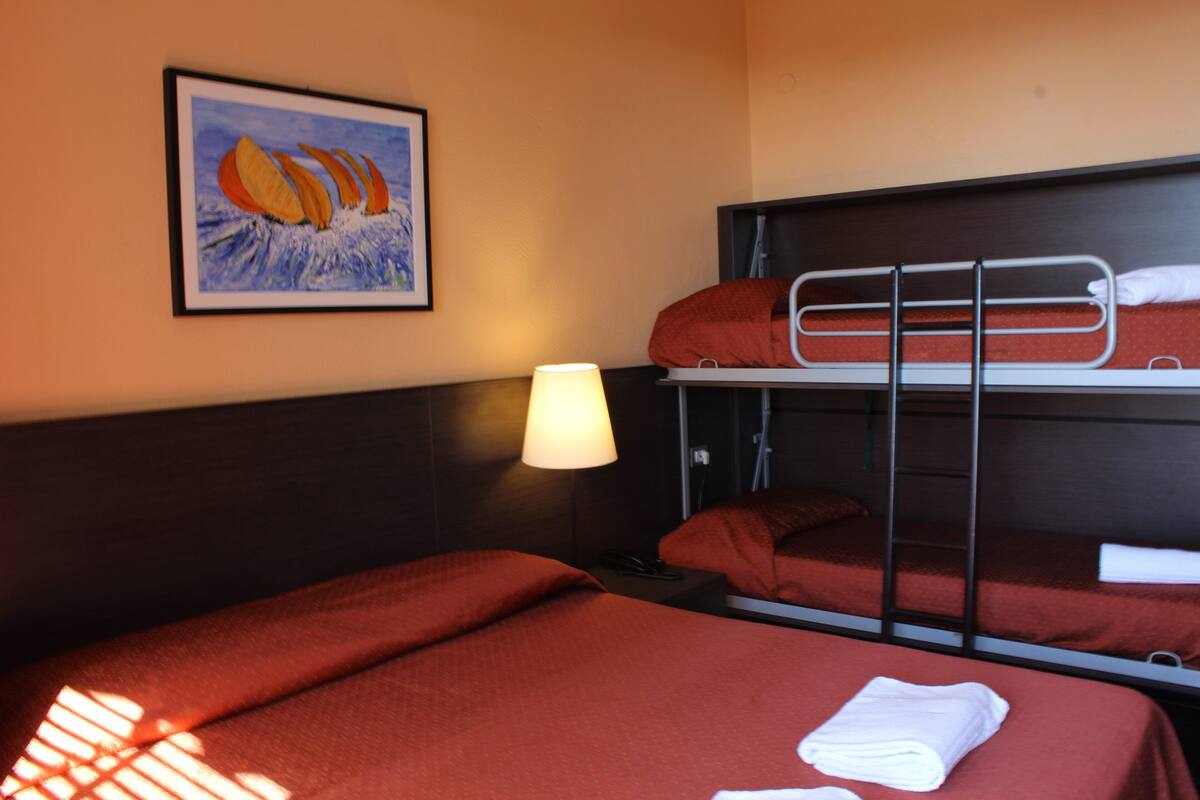 A hotel room with a bunk bed, a single bed, a bedside lamp, and a framed picture on the wall.