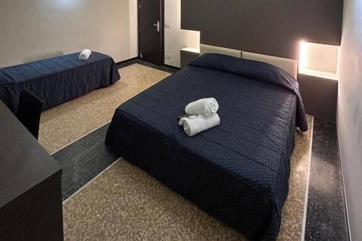 A hotel room with a large bed, two smaller beds, a desk, and a door.
