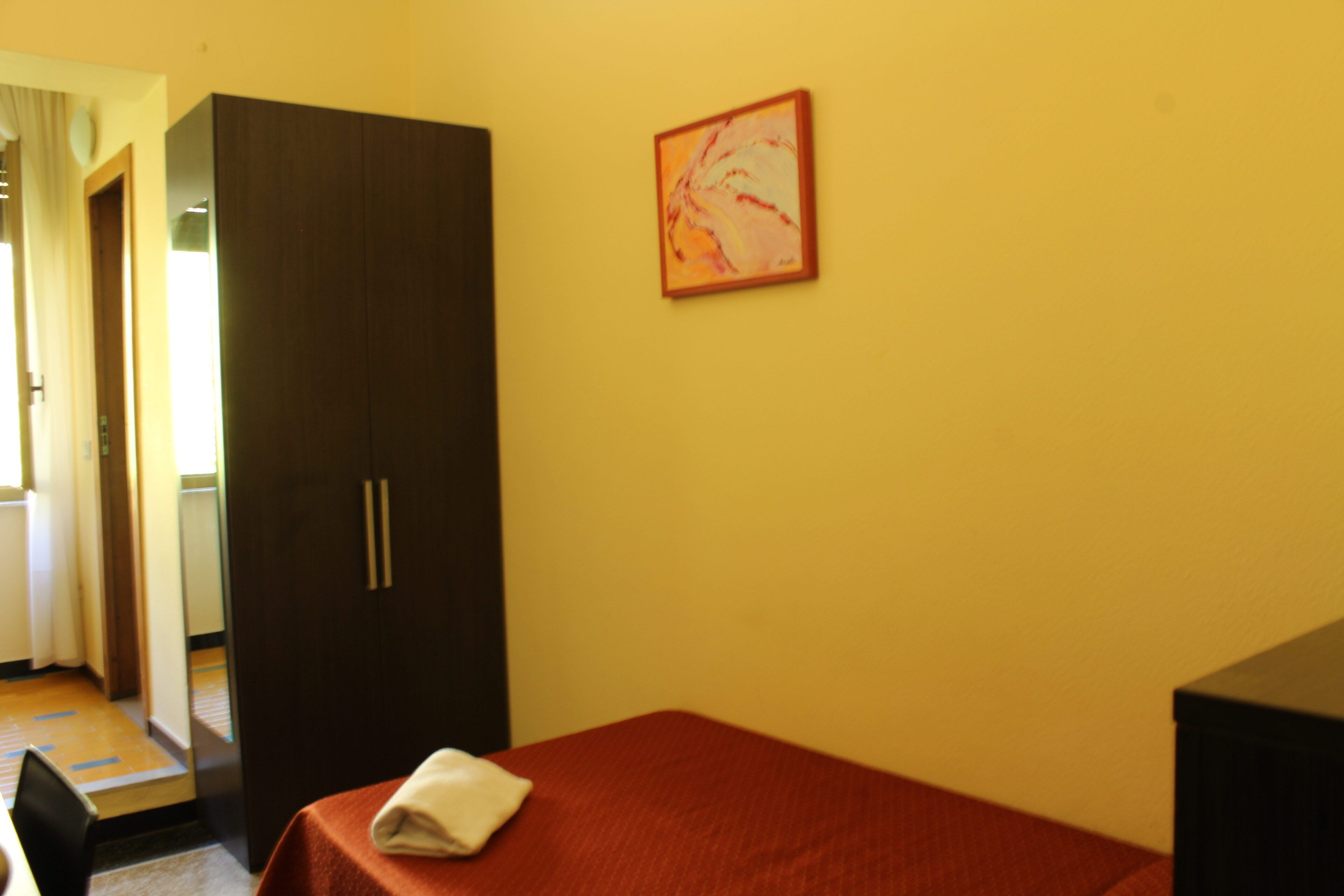 Una camera d'albergo con un letto, un armadio, un quadro appeso e una porta che dà su un'altra stanza.