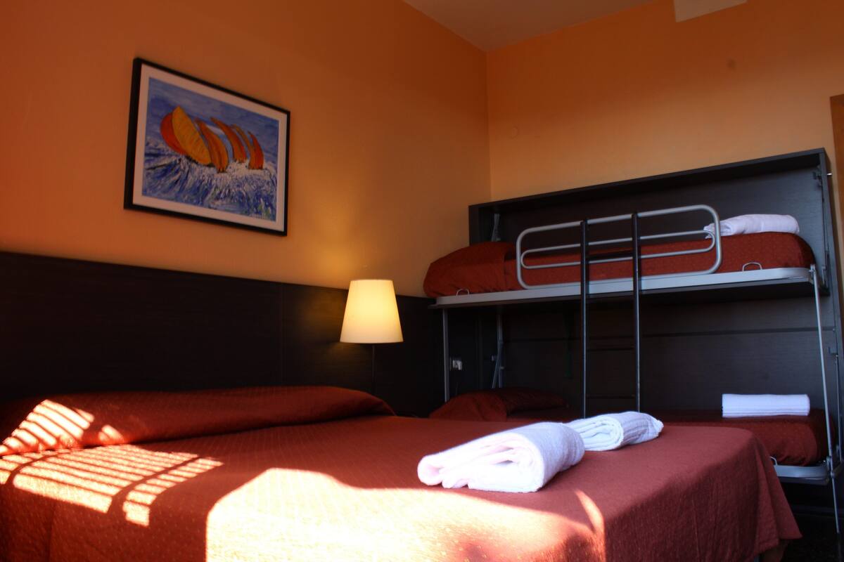 A hotel room with a bunk bed, a single bed, a framed picture on the wall, and a lamp.