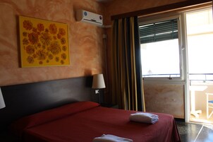 Habitación de hotel con cama, aire acondicionado, lámpara, ventana con cortinas y vista al exterior.