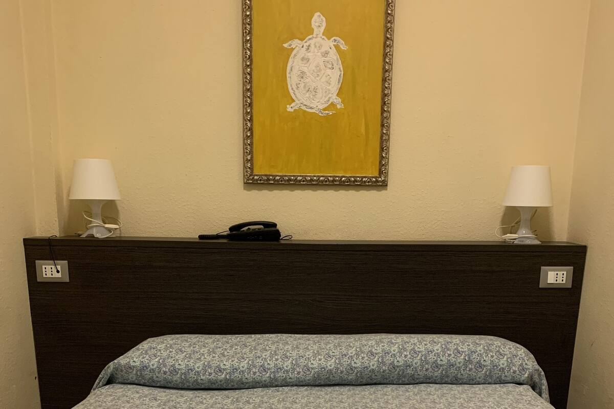 A hotel room with a bed, two bedside lamps, a phone, and a framed artwork on the wall.