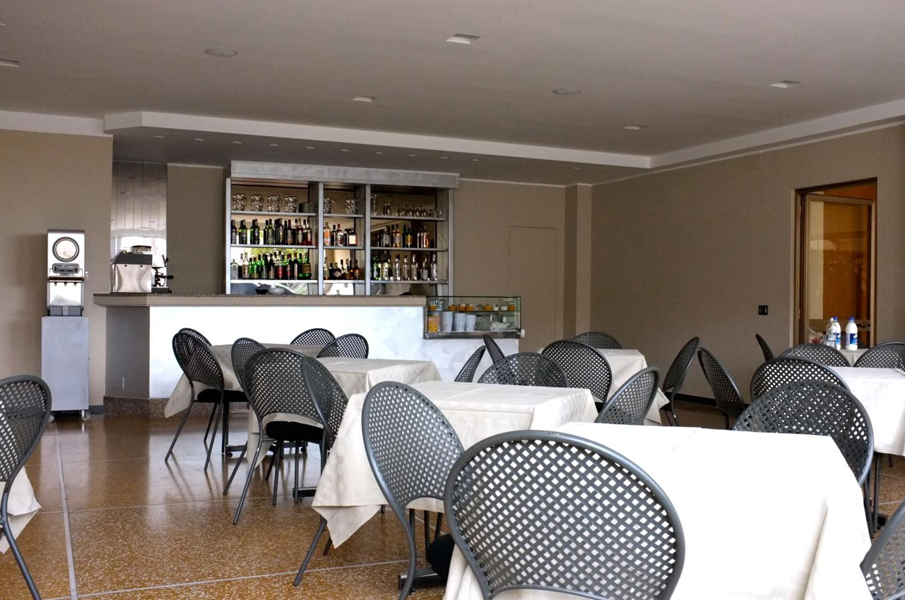 Ein Restaurant mit Tischen und Stühlen, eine Bar mit Regalen voller Flaschen und ein Kühlschrank.