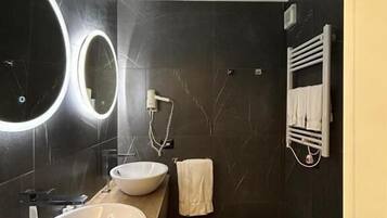 A modern bathroom with a large mirror, two sinks, a toilet, and a towel rack.