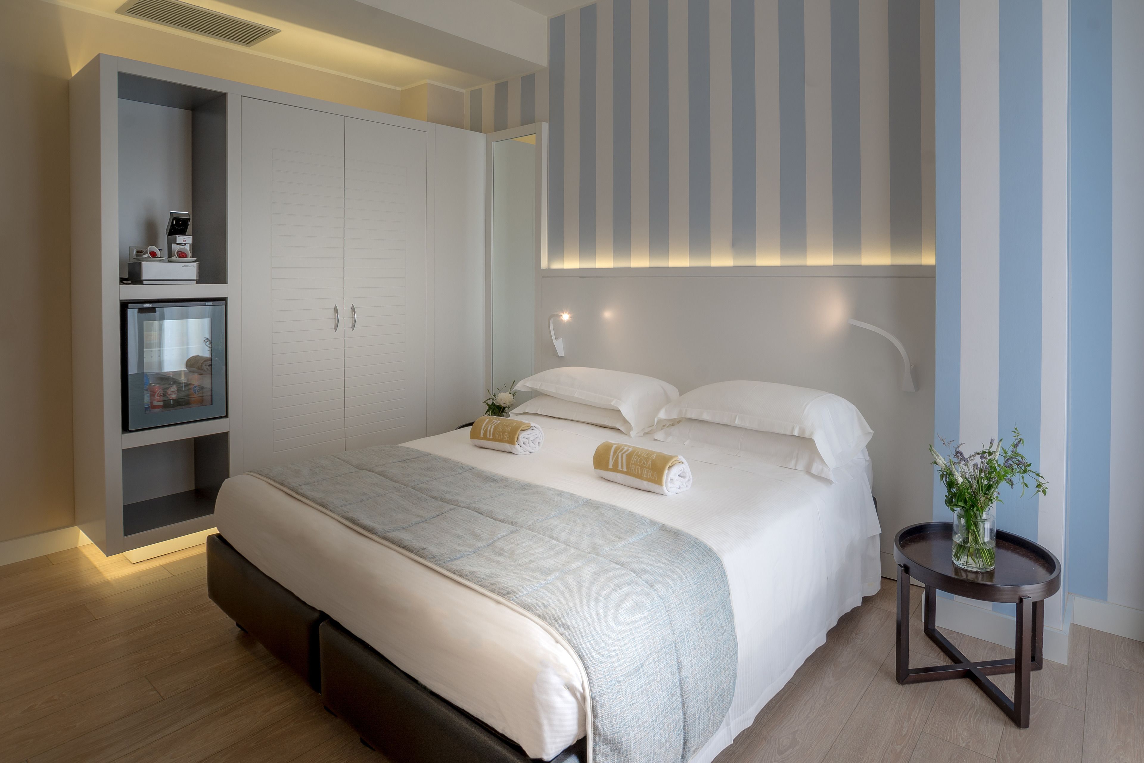 A modern bedroom with a large bed, a bedside table with a vase, and a wardrobe with shelves.