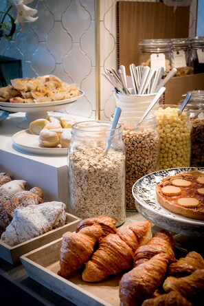 A buffet with various pastries, including croissants and muffins, and jars of oats and other grains.