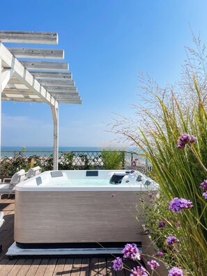 A hot tub with a wooden deck and a pergola, overlooking a beach.