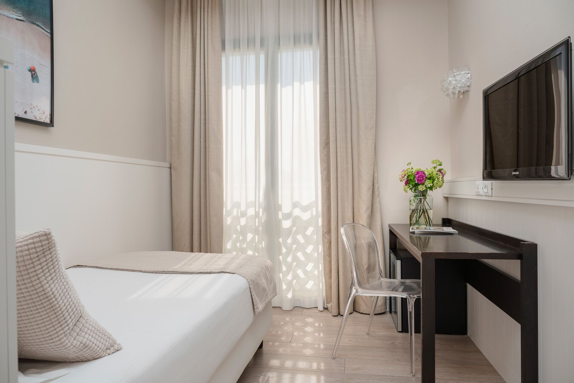 Habitación de hotel con cama, escritorio con silla, televisión y ventana con cortinas.