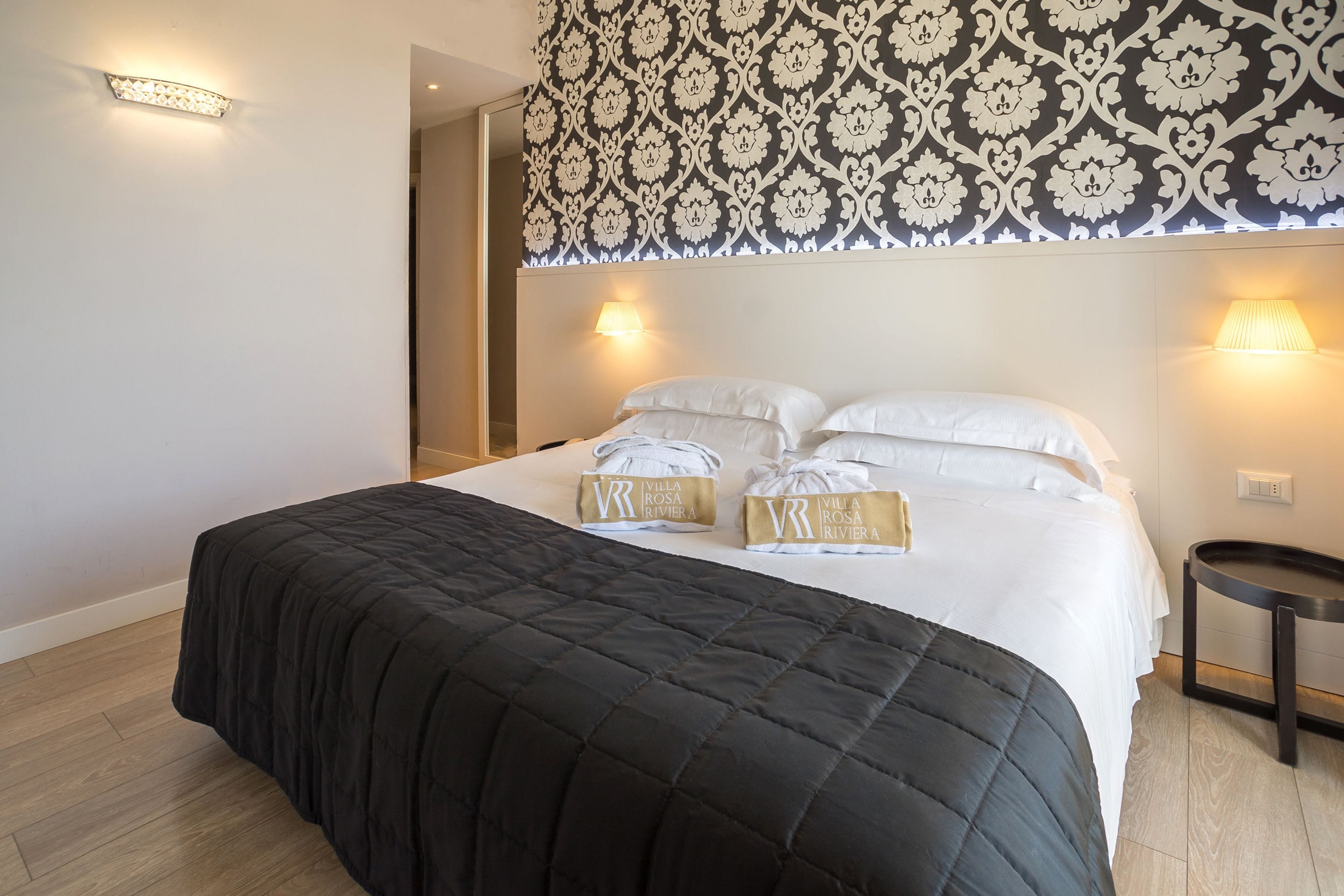 A hotel room with a large bed, two bedside lamps, a small round table, and a patterned wallpaper.