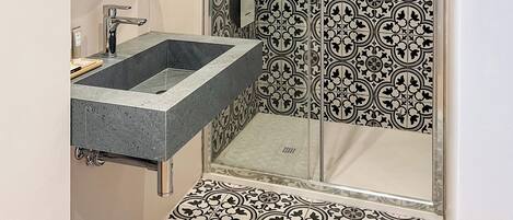 Un baño moderno con ducha envuelta en vidrio, lavabo con encimera de mármol y azulejos estampados en paredes y suelo.