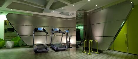 Un gimnasio moderno con cintas de correr, una bicicleta estática y una pared verde.