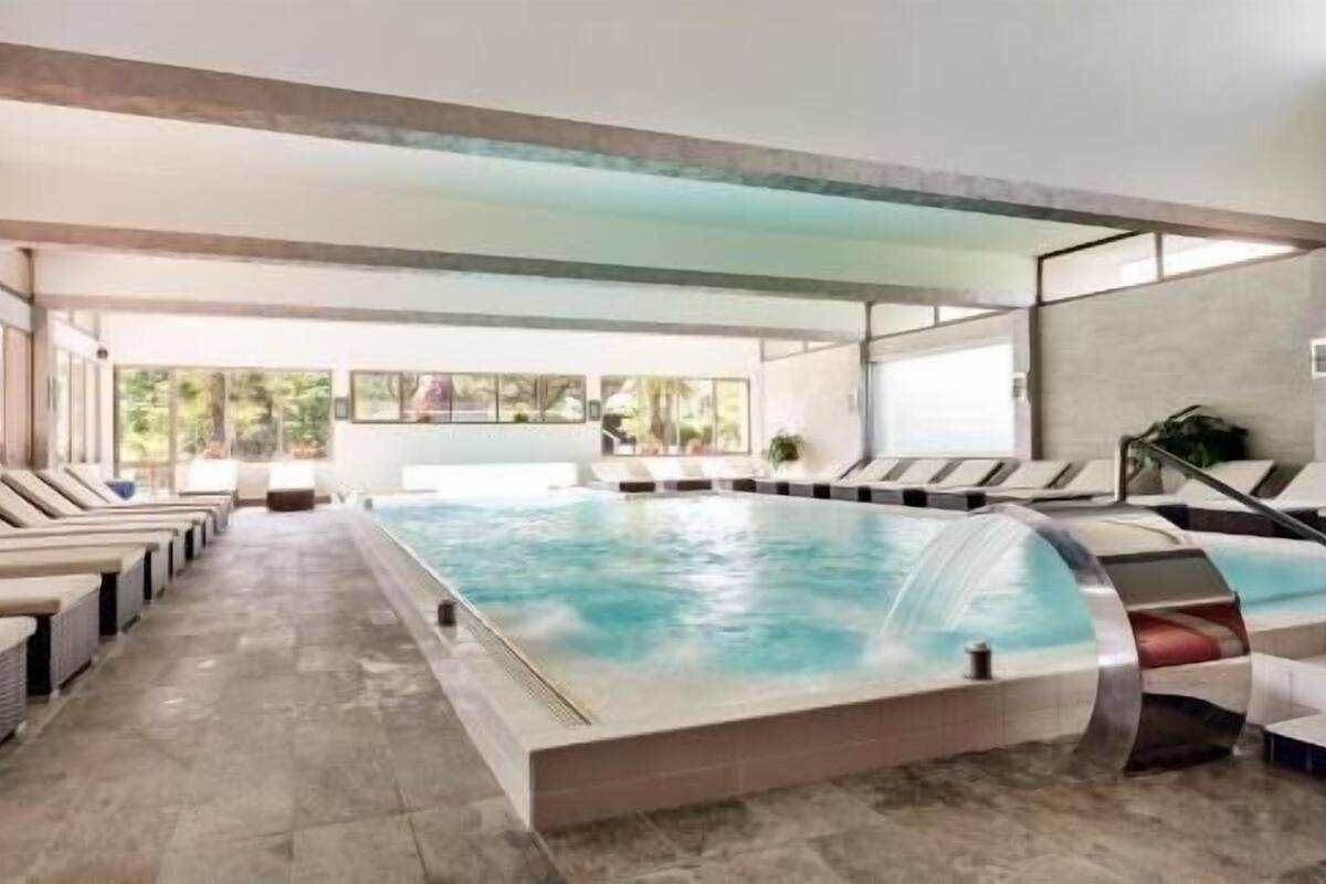 Una amplia piscina cubierta con sillones reclinables y vistas a zonas verdes.