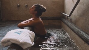 Una persona sentada en una bañera, con una toalla al lado.