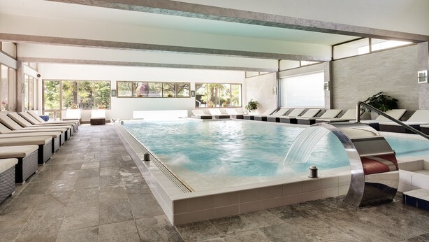 Un área de piscina interior moderna con sillones de descanso, una gran piscina y vistas al exterior.