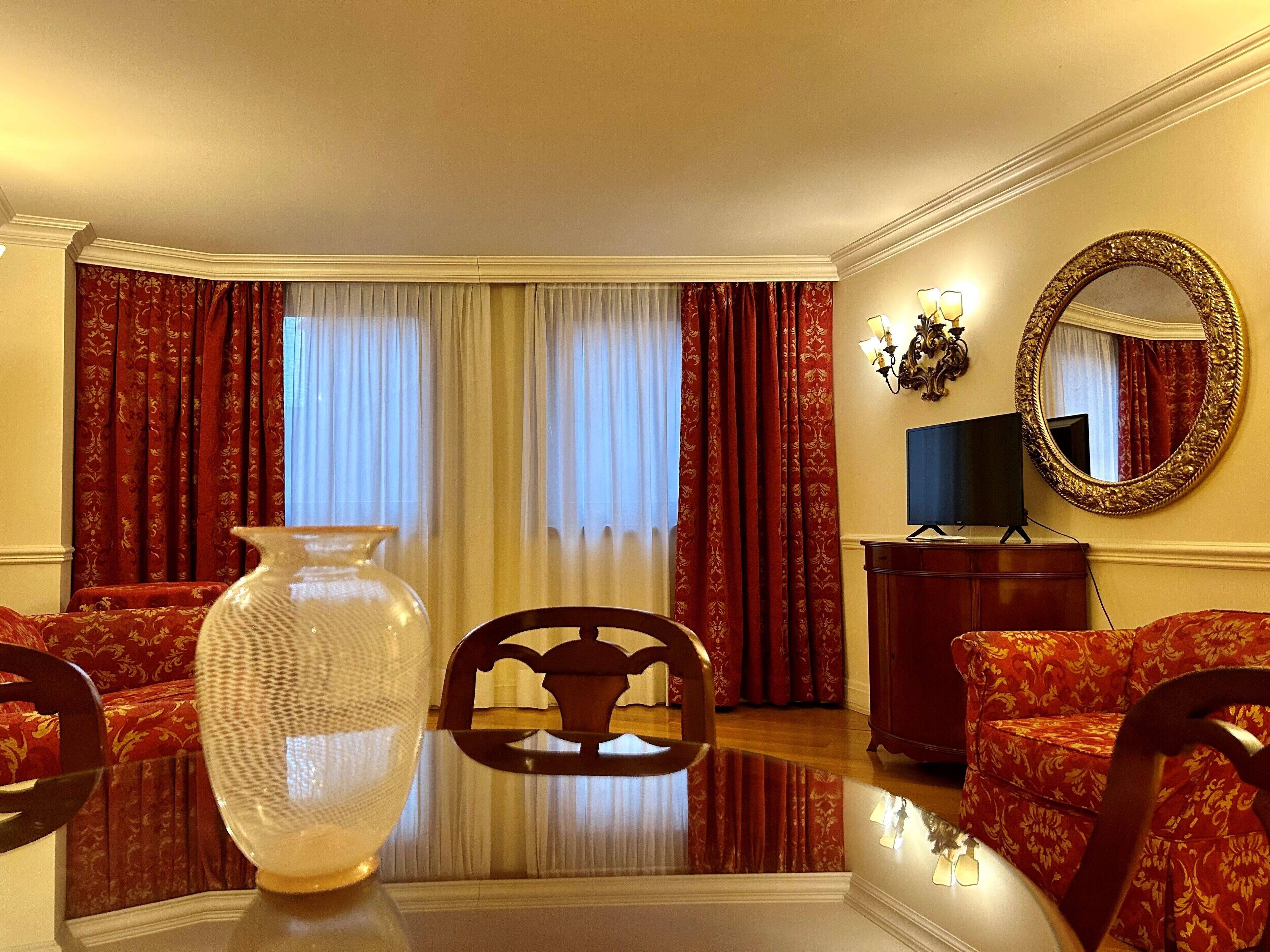 Una camera d'albergo con un vaso grande, due divani, una TV e uno specchio a parete.
