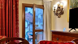 A hotel room with a dining table, chairs, a red vase, a TV, and a view of the outside balcony. - TORRE DELL'OROLOGIO SIGNATURE RESIDENCE (Venice)
