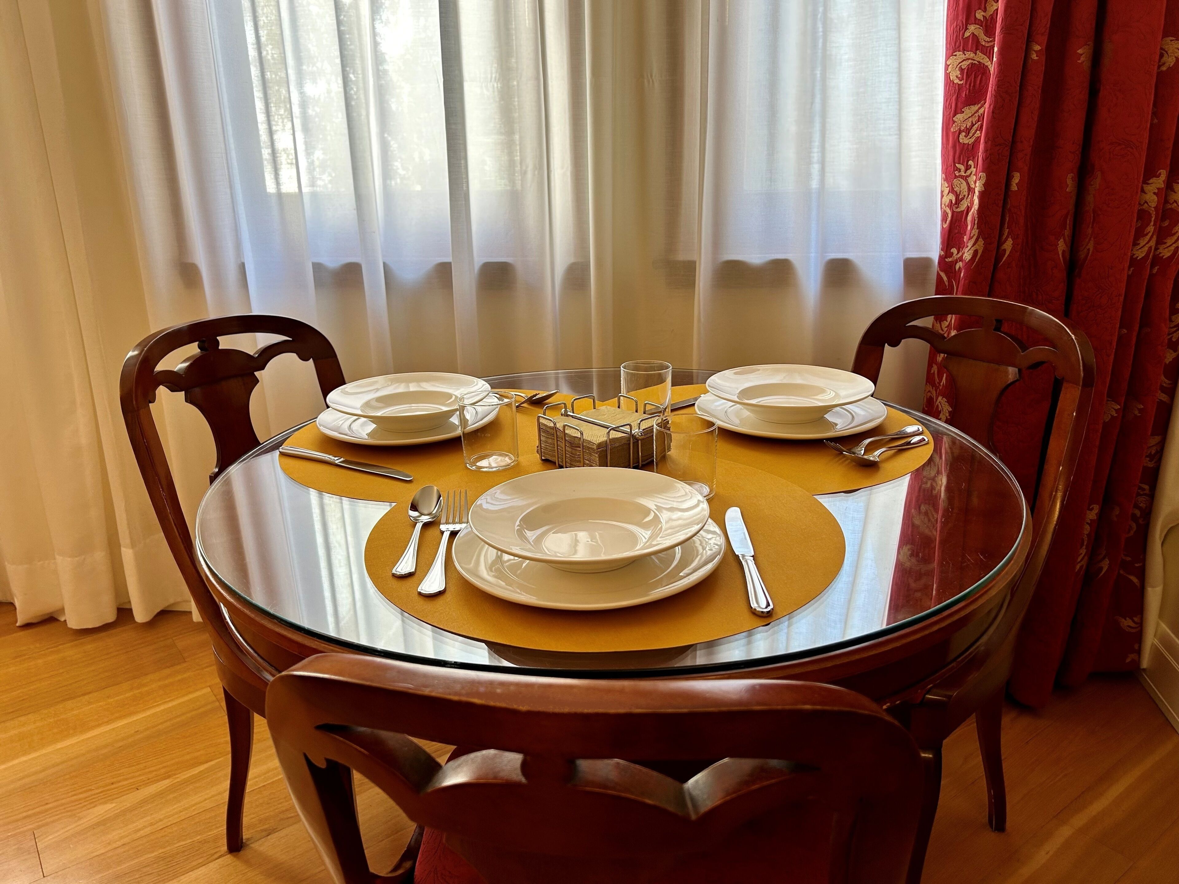 Una mesa redonda de vidrio con un mantel individual amarillo, rodeada de sillas de madera.