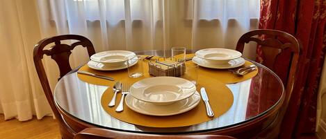 Una mesa redonda de vidrio con un mantel individual amarillo, rodeada de sillas de madera.