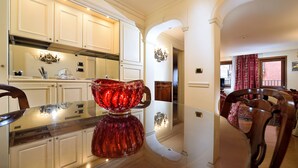 A modern kitchen with white cabinetry, a glass-top dining table, and a red decorative bowl. - TORRE DELL'OROLOGIO SIGNATURE RESIDENCE (Venice)