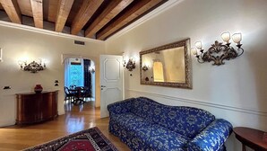 A spacious living room with a blue patterned sofa, a red patterned rug, wooden beams on the ceiling, a large mirror, and a dining area with chairs and a table. - TORRE DELL'OROLOGIO SIGNATURE RESIDENCE (Venice)
